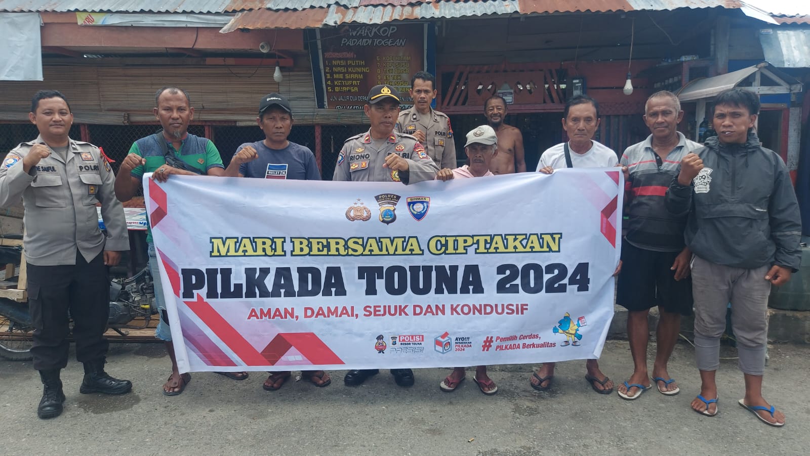 melalui spanduk dan stiker mari bersama-Sama Ciptakan Pilkada Touna 2024, Aman, Damai, Sejuk Dan Kondusif