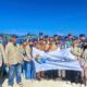 Suasana dokumentasi bersama Bupati Tojo Una-Una Ilham Lawidu, pejabat daerah, perangkat desa, dan 28 mahasiswa peserta KKN-PPM Universitas Gadjah Mada Gelombang II Tahun 2026 di salah satu lokasi pesisir Kecamatan Togean, Senin (22/6/2026). Dengan latar belakang keindahan alam kepulauan, rombongan memperagakan bendera bertuliskan Ekspedisi Togean, menandai dimulainya pengabdian masyarakat selama 50 hari.